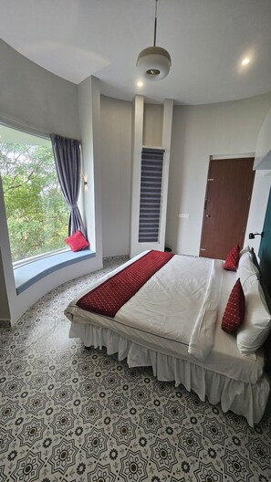 A bedroom with a large bed, a window with curtains, a door, and a patterned floor.