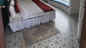 Un dormitorio con cama, ventana con vistas, ventilador de techo y suelo estampado.