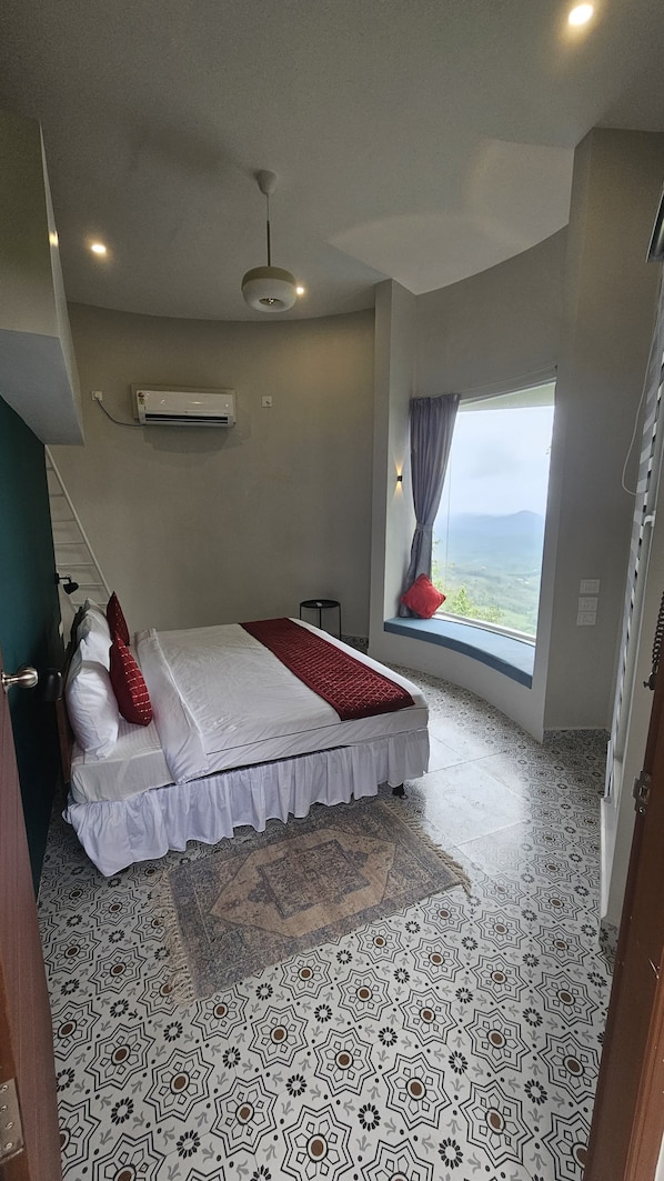 A bedroom with a bed, a window with a view, a ceiling fan, and patterned flooring.
