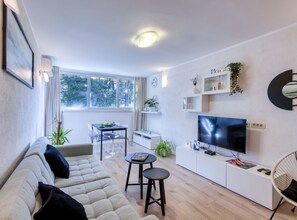 Ein modernes Wohnzimmer mit Sofa, Esstisch, Fernseher und Bücherregal.