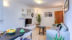 A modern living room with a dining area, a flat-screen TV, a bookshelf, and a wooden door. - Apartment Promenada (Dubrovnik)