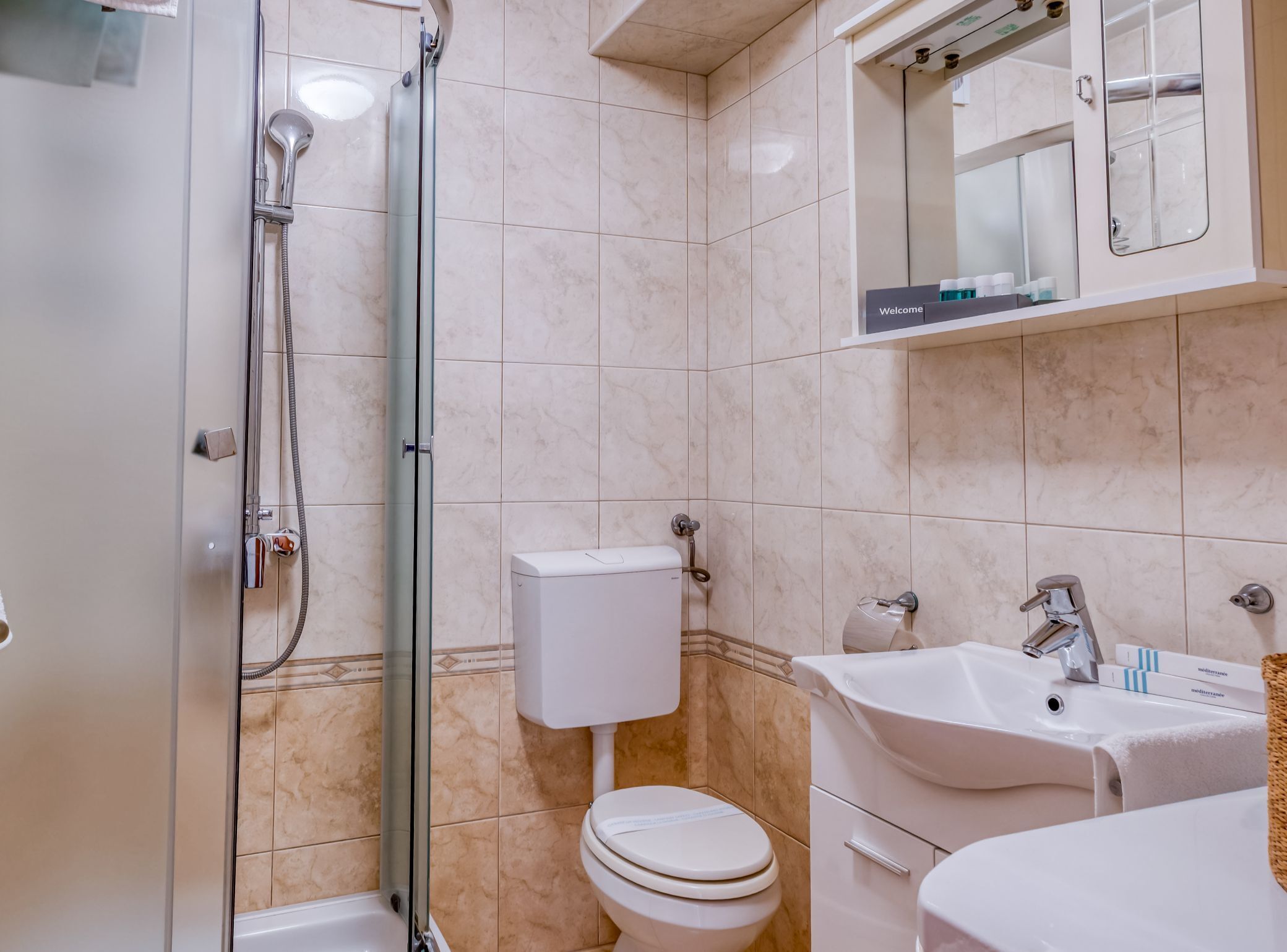 Et moderne badeværelse med glasvæg omkring bruseren, toilet, håndvask og spejl.
