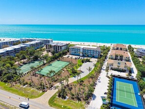 Un hôtel situé sur la côte, composé de plusieurs bâtiments, doté de courts de tennis et offrant une vue sur la plage.