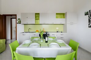 Een moderne keuken met witte kasten, een eethoek met een tafel voor vier personen, en een groene accentmuur.
