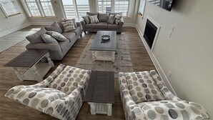A spacious living room with a grey sectional sofa, a coffee table, and patterned ottomans. - Waterfront Seclusion Stunning Sunsets and Golf! (Jarvisburg)