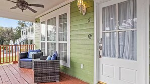 Varanda com móveis de vime, um ventilador de teto e uma porta verde com a placa de identificação '2'.