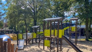 A playground with yellow and brown play structures, including slides and climbing areas, set in a sandy area with trees in the background. - Chatel Studio voor 2 personen | Resort de Heimolen (Baarle-Nassau)