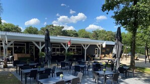 An outdoor patio area with tables and chairs, a covered seating area, and a flag. - Chatel Studio voor 2 personen | Resort de Heimolen (Baarle-Nassau)