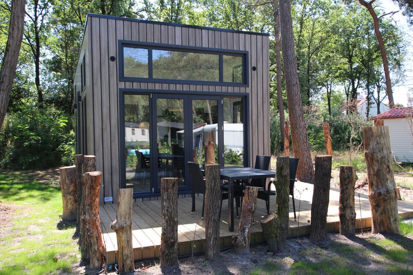 A modern wooden cabin with large windows, a deck, and a table with chairs.