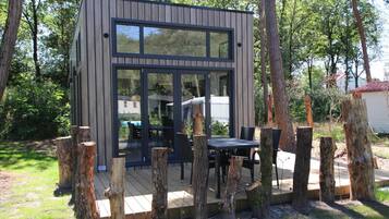 A modern wooden cabin with large windows, a deck, and a table with chairs.