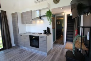 Moderni keittiö, jossa on harmaat kaapit, sisäänrakennettu uuni ja kahvinkeitin. Portaat johtavat olohuoneeseen, jossa on sohva ja viherkasvi.