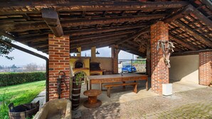 Eine Terrasse im Freien mit Kamin aus Backstein, einem Holztisch und Bänken.