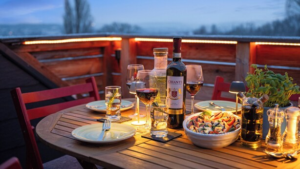 Ein Holztisch, gedeckt für eine Mahlzeit, mit Weingläsern, einer Chianti-Flasche und einer Salatschüssel.