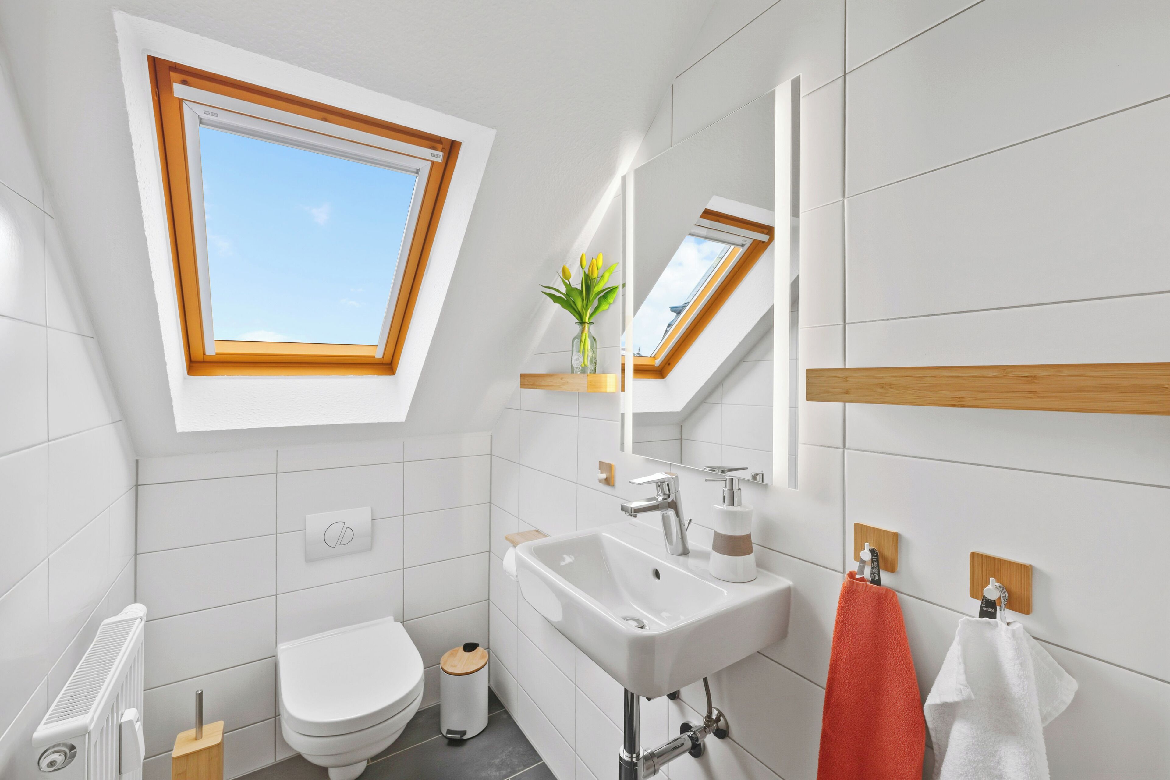 A modern bathroom with a skylight, white tiles, a white sink, and a toilet.