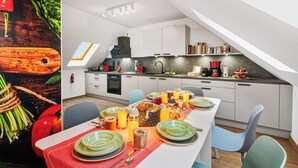 Eine moderne Küche mit weißen Schränken, einer schwarzen Dunstabzugshaube und einer Frühstücksecke mit Tellern, Gläsern und einer Obstschale.