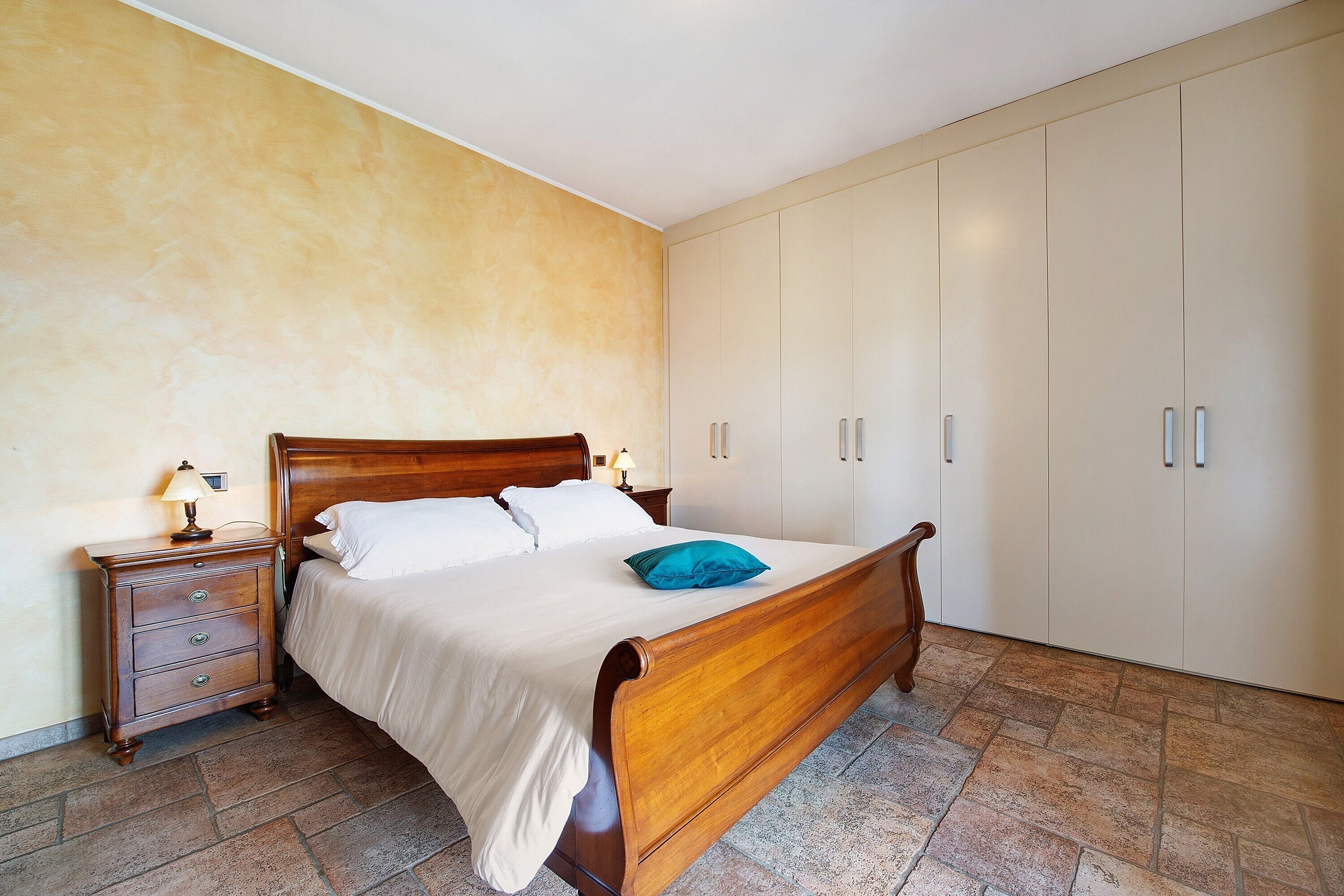 A bedroom with a wooden bed, a nightstand, a lamp, and a wardrobe.