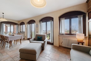 A spacious room with a dining table, two sofas, and large windows with curtains.