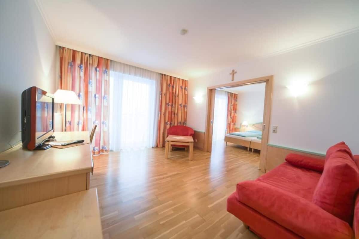 Um quarto com uma escrivaninha de madeira, um sofá vermelho, uma cama com colchão azul e uma mesinha.