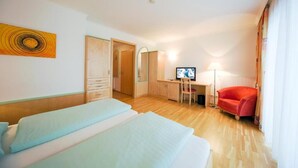 Une chambre d’hôtel avec deux lits, un bureau avec un ordinateur, une télévision et une chaise rouge.