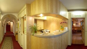 Un espace d’accueil avec un comptoir en bois incurvé, une plante en pot et une enseigne indiquant « Gaststube ».