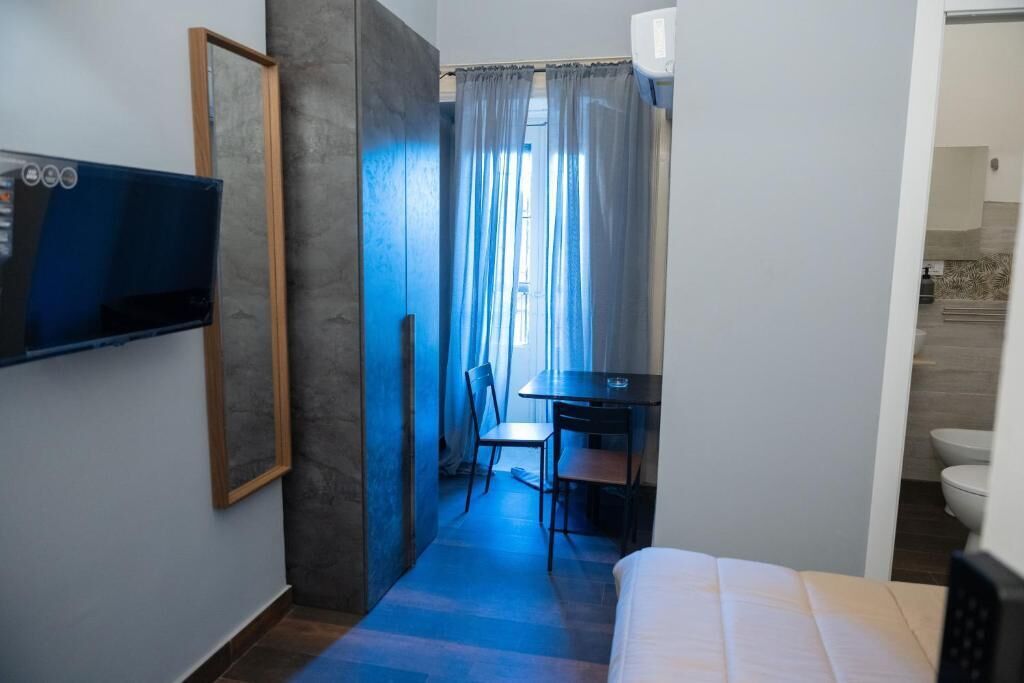 Une chambre d’hôtel avec un lit, un bureau et une chaise. Il y a un téléviseur fixé au mur et une fenêtre avec des rideaux.