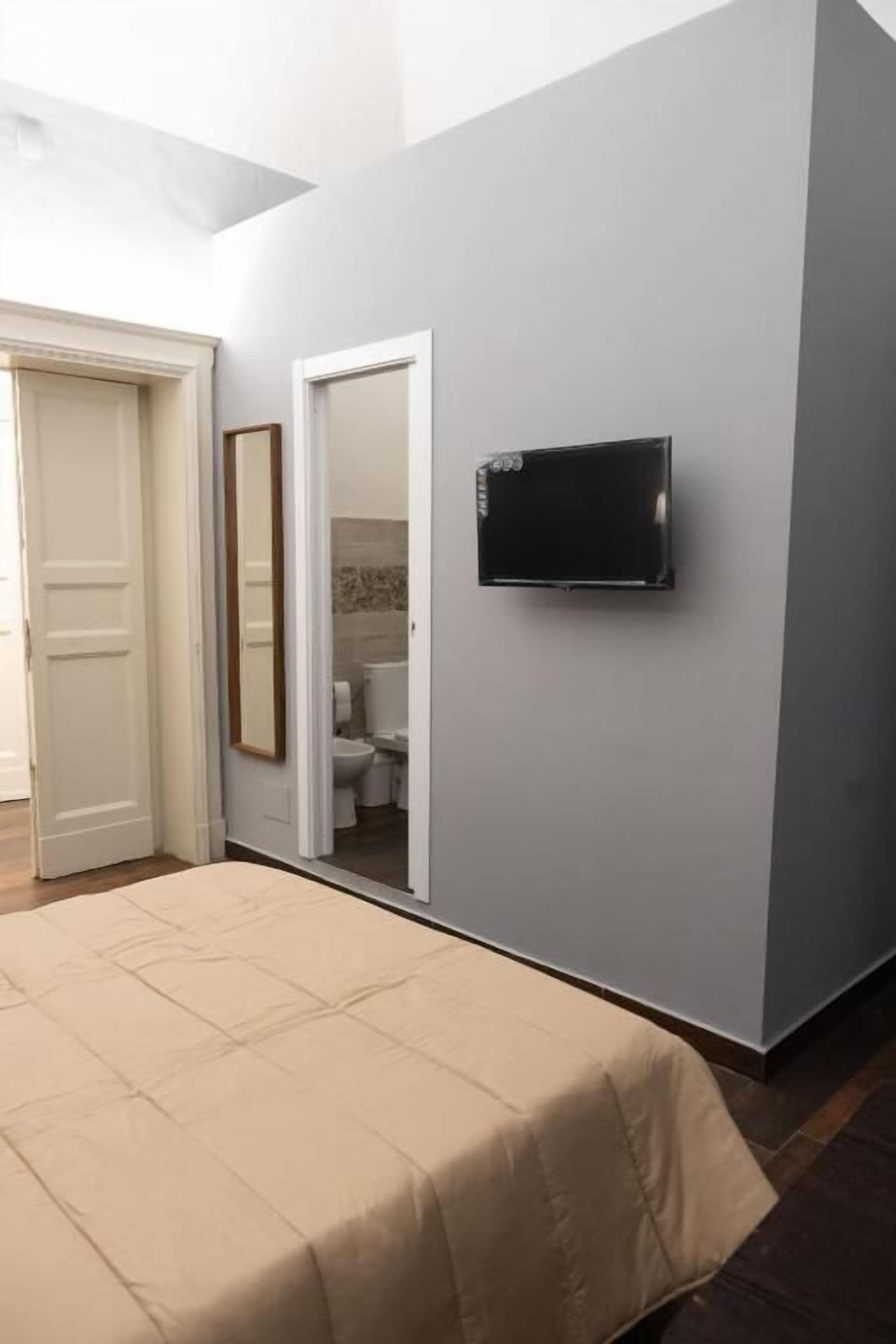 A bedroom with a bed, a television mounted on the wall, and a door leading to a bathroom.
