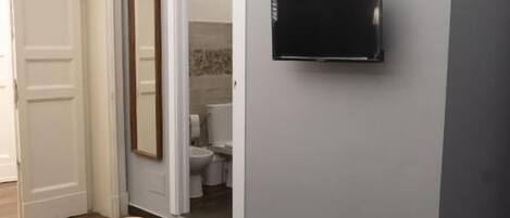 A bedroom with a bed, a television mounted on the wall, and a door leading to a bathroom.