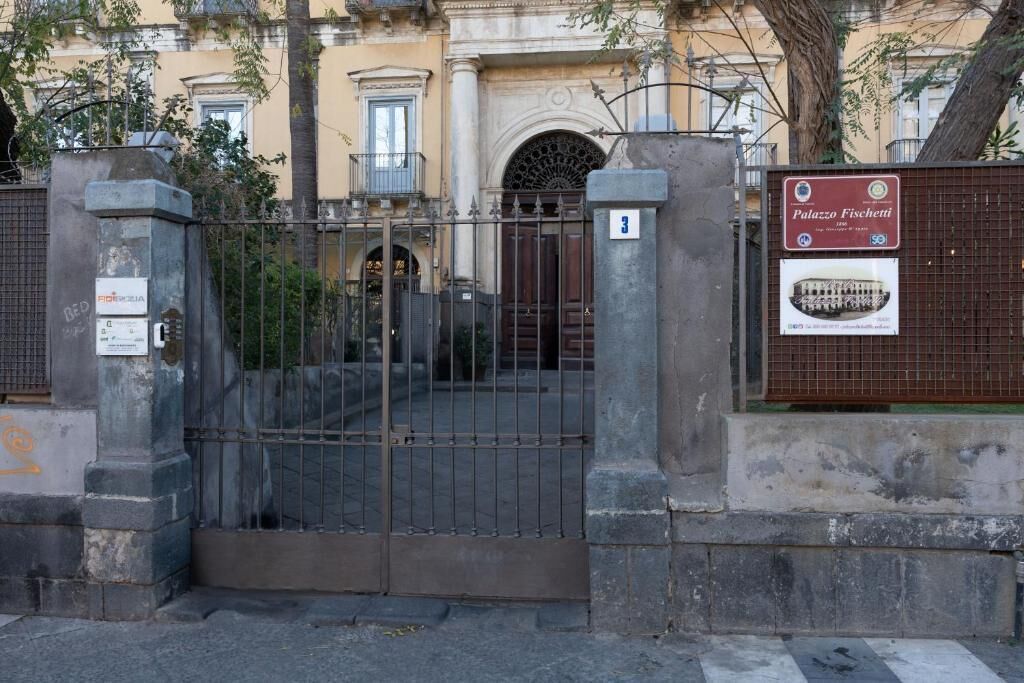 Une entrée fermée par un portail mène à un immeuble sur lequel est apposée une plaque indiquant « Palazzo Fischetti ».