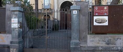 Une entrée fermée par un portail mène à un immeuble sur lequel est apposée une plaque indiquant « Palazzo Fischetti ».