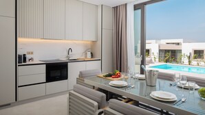 A modern kitchen with a dining area, a view of a swimming pool, and a large window. - The Palms Resort 2BR Villa Dream Four with Pool (Tkon)