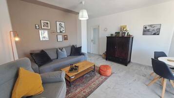 Una sala moderna con un sofá gris, una mesa de centro de madera, un mueble oscuro y un comedor con mesa y sillas blancas.