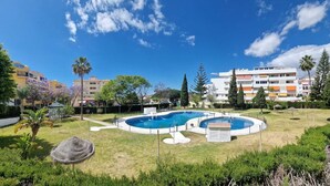 A swimming pool surrounded by a grassy area with trees and a multi-story building in the background. - New!! Enjoy Benalmadena Costa!! Magnificent views, 2 bedrooms, terrace, garage (Benalmádena)