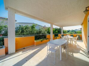 A covered outdoor patio with a table and chairs, surrounded by orange walls and greenery.