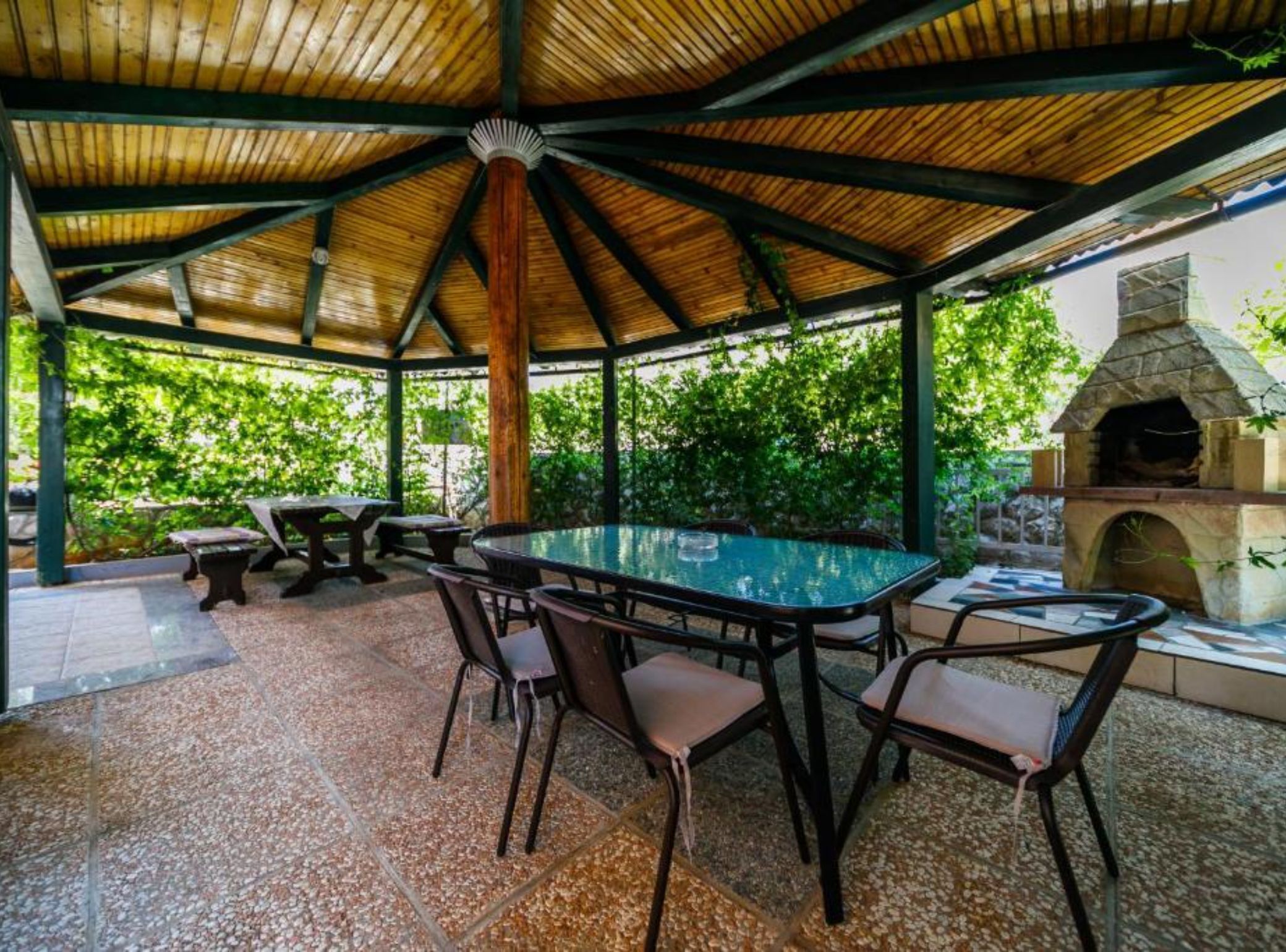 An outdoor patio with a glass-top table and chairs, surrounded by a wooden pergola.