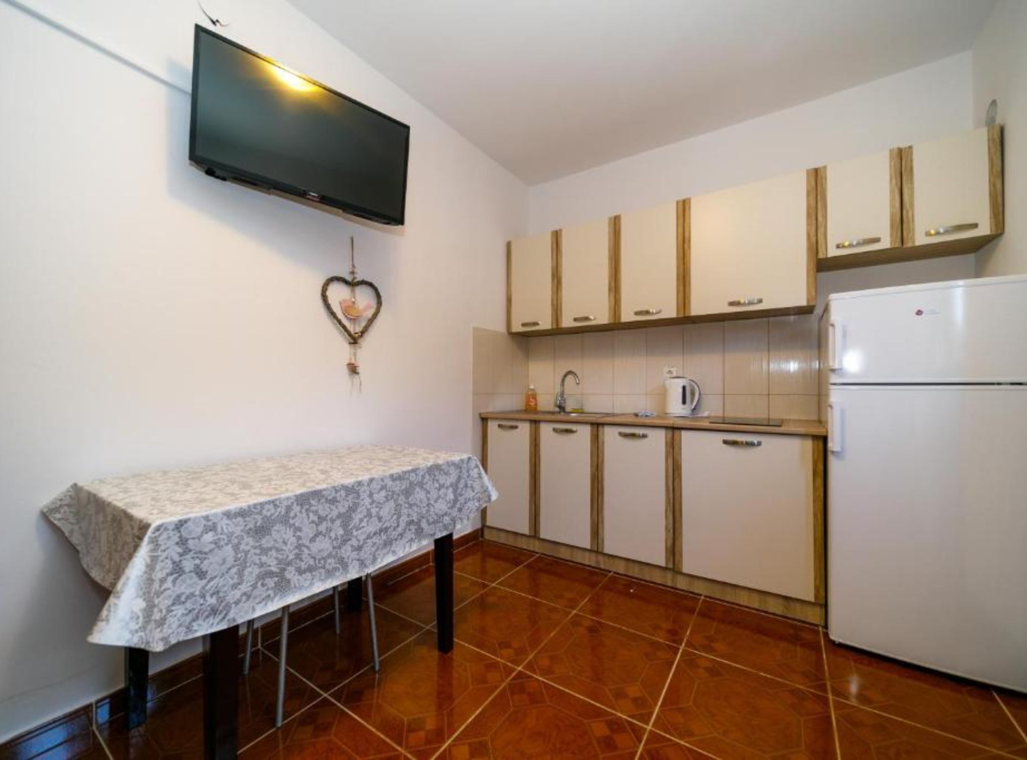 A small kitchen with a tiled backsplash, a white refrigerator, a coffee maker, and a heart-shaped decoration on the wall.