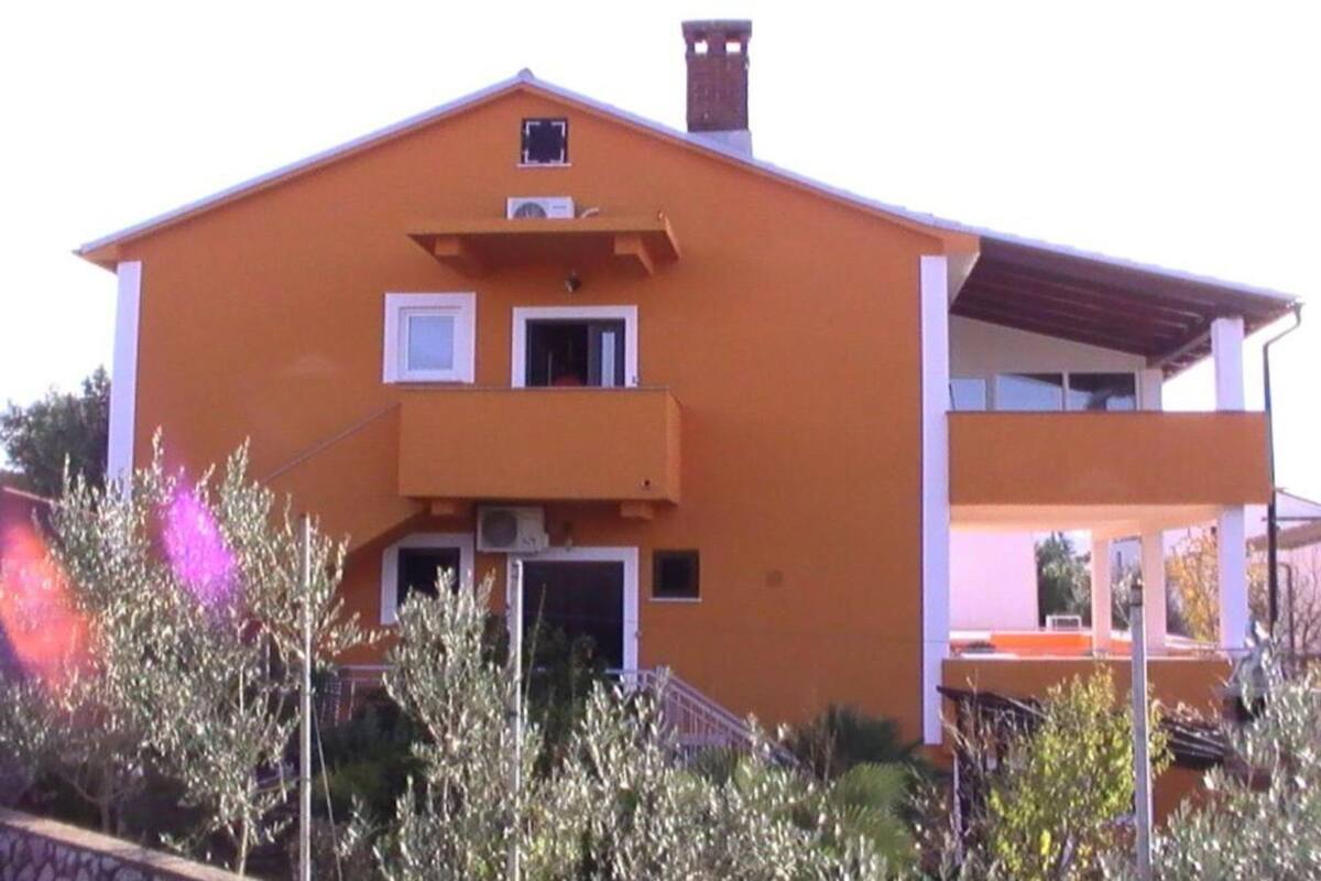 A two-story building with a flat roof, a balcony on the second floor, and a chimney on the roof.