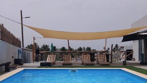A rectangular swimming pool with a clear blue water surface, surrounded by a wooden deck with lounge chairs. - Room-serene Apartment Escape in Achada F (Santa Cruz)