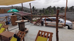 A rooftop patio with wooden furniture, a table with a pot, and a car parked in the background. - Room-serene Apartment Escape in Achada F (Santa Cruz)
