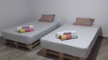 Two single beds with wooden pallets, white bedding, and colorful towels.