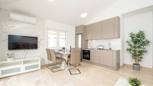 Eine moderne Küche mit Einbauofen, ein Essbereich mit Tisch und Stühlen, ein an der Wand befestigter Fernseher und ein Topfpflanze.