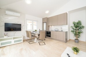 A modern kitchen with a built-in oven, a dining area with a table and chairs, a TV mounted on the wall, and a potted plant. - Two-bedroom apartment Pulse with poolside patio and sea view (Novalja)