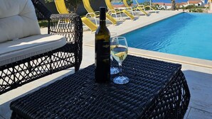 Ein Poolbereich mit Korbmöbeln, einer Weinflasche und einem Glas.