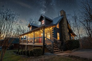 Une cabane en rondins dotée d’un balcon, d’une cheminée en pierre et de guirlandes lumineuses.