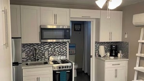 Una cocina compacta con armarios blancos, un microondas de acero inoxidable, una estufa a gas y un salpicadero de azulejos.
