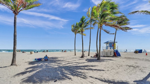Una playa con palmeras, una torre de salvavidas y sillas de playa.