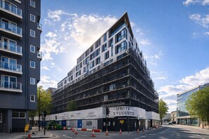 Un edificio de varios pisos con un diseño arquitectónico moderno, que presenta un llamativo cartel de 'UNITE STUDENTS' a nivel de la planta baja.