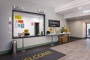 Un espace d’accueil avec un paillasson, un panneau d’affichage où sont affichées diverses informations et une pancarte indiquant « Faites connaissance avec votre équipe ».