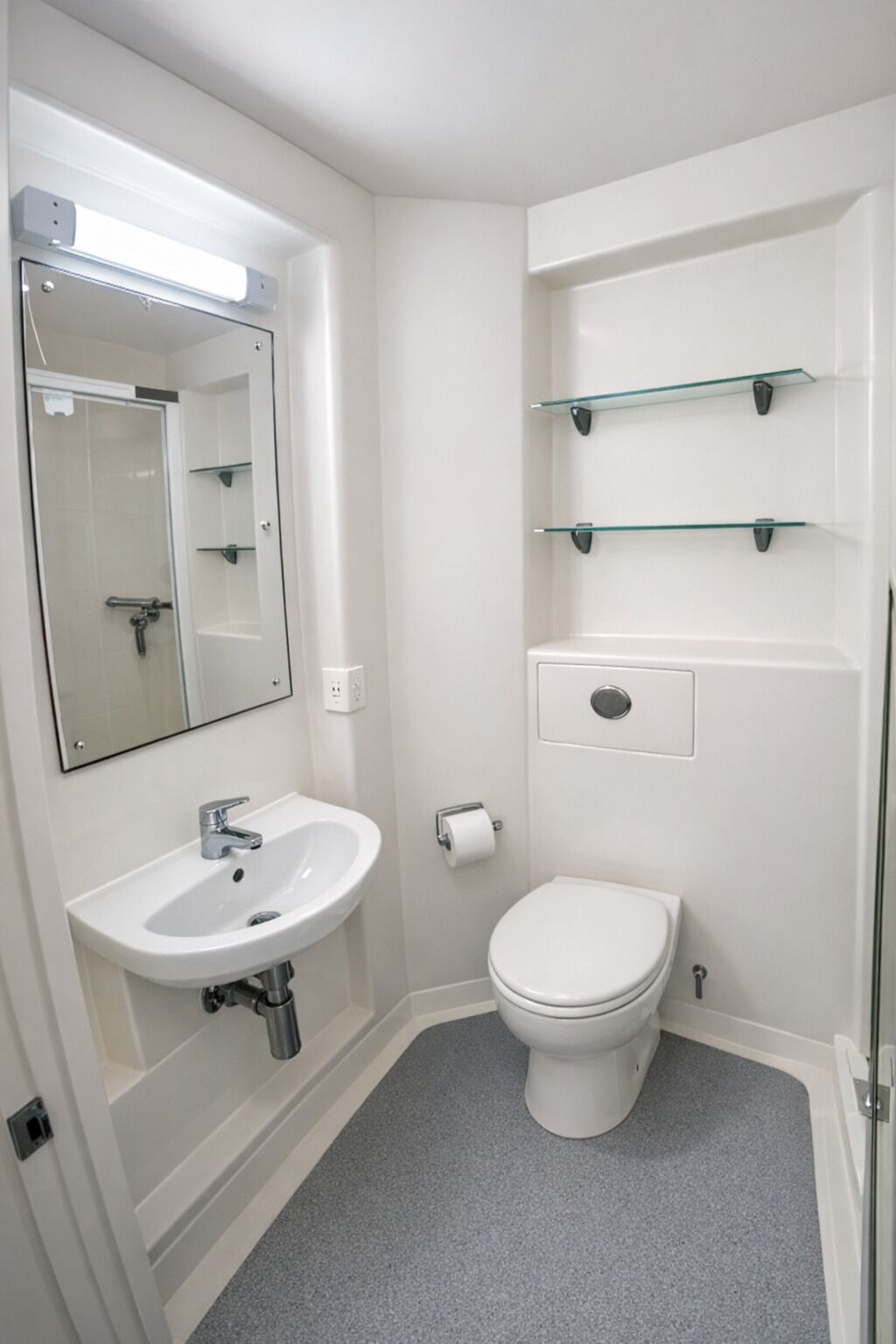 Une salle de bain avec un lavabo blanc, un miroir, des toilettes et des étagères en verre.