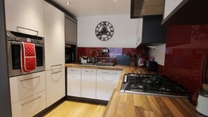 A modern kitchen with white cabinets, a red oven, a gas stove, and a wall clock.