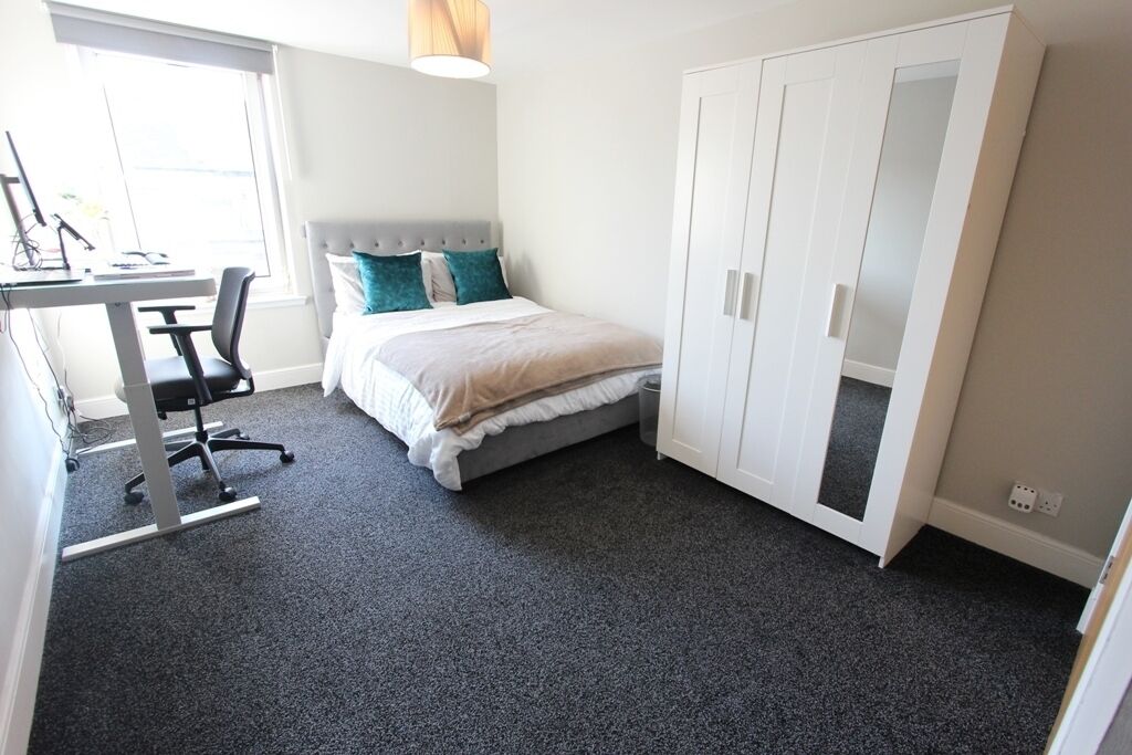 A bedroom with a bed, a desk, and a wardrobe.